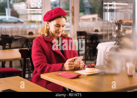 Elegante signora matura indossando cappotto rosso seduto in intimo cafe Foto Stock