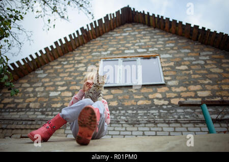 Sloviansk, Ucraina. 29 ott 2018. Kira Romanova giocando con un piccolo gatto di fronte alla casa di famiglia in un villaggio vicino a Sloviansk. La loro casa di proprietà e sono stati gravemente danneggiati in seguito a conflitti tra il militare ucraino e pro-russo separatisti in Ucraina orientale e in parte ricostruito e rinnovato dal tedesco di aiuti allo sviluppo. Credito: Gregor Fischer/dpa/Alamy Live News Foto Stock