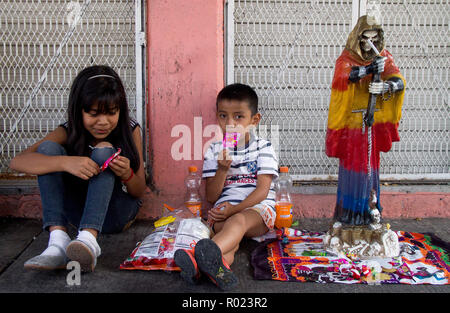 Il 31 ottobre 2018, Messico Città del Messico: Bambini mangiare dolci accanto alla statua di Santa Muerte nel quartiere di Tepito. I seguaci dei santi patroni offrono Santa Muerte sacrifici come caramelle, mele o agave schnapps in occasione del Giorno dei Morti. A Città del Messico, centinaia di sostenitori fecero offerte per la santa patrona Santa Muerte in occasione del 'Día de los Muertos' ('Day dei morti"). Le persone si sono radunate mercoledì 31.10.2018 presso il Santuario dei Santi nel quartiere di Tepito. Santa Muerte - in tedesco "santa morte' - è rappresentato da uno scheletro che indossa frocks o w Foto Stock