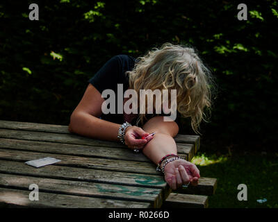 Una donna di iniettare il farmaco nel suo braccio con una siringa in strada e una dose di farmaco per lato Foto Stock
