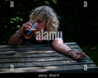 Una donna con un gran numero di pillole in mano di diversi colori e dimensioni e un bicchiere di birra a un tavolo per esterno Foto Stock