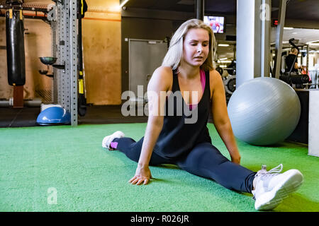 Montare la giovane donna presso la palestra facendo davanti split esercizio. Atleta femminile in una sala fitness che lavora fuori sulla gamba split Foto Stock