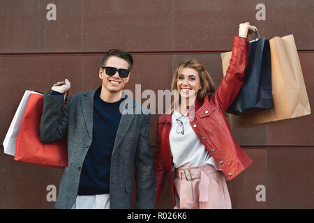 Giovane e bella coppia amorevole il trasporto delle borse della spesa e godendo insieme. Immagine che mostra la coppia giovane di shopping in citta'. Foto Stock