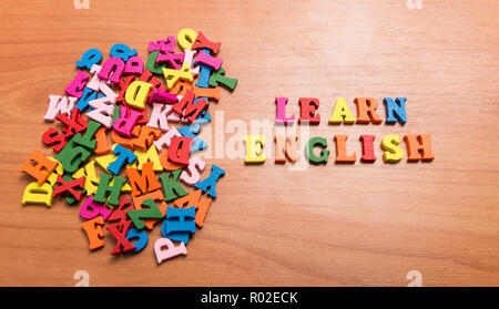 Impara Inglese messaggio in lettere di legno vicino a un mucchio di altre lettere su office sfondo tabella Foto Stock