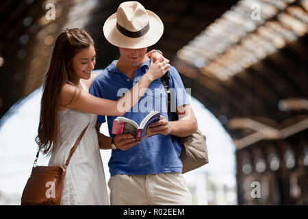 Venti qualcosa di giovane leggere un libro guida in corrispondenza di una stazione ferroviaria. Foto Stock