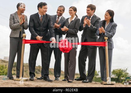 I giovani imprenditori di applaudire come il loro collega taglia un nastro rosso nel corso di una cerimonia per iniziare un nuovo progetto di costruzione. Foto Stock