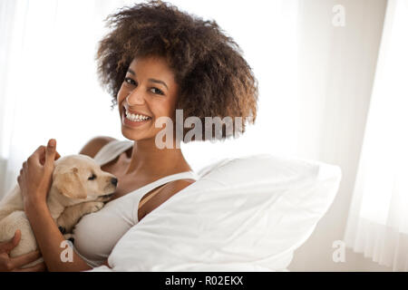 Donna pacche un cucciolo da seduto sul letto. Foto Stock