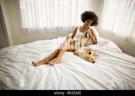 Giovane donna ascoltando il suo iPod mentre è seduto sul letto con sleeping Labrador cuccioli. Foto Stock