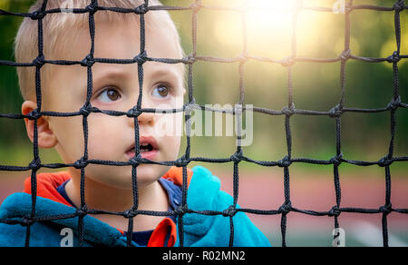 Carino giovane ragazzo caucasico guardando attraverso il tennis net in primavera Foto Stock