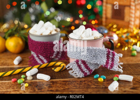Due tazze in accoglienti sciarpe con una calda bevanda dolce e marshmallows. Close-up. Foto Stock