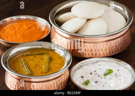 Freschi cotti al vapore folli indiano (Idli / Torta di riso) disposti in autentica ciotola di rame. Servita con chutney di pomodoro, chutney di cocco e sambar. Foto Stock