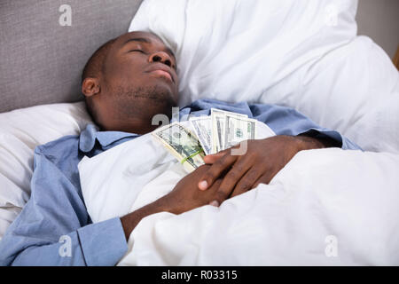 L'uomo africano che dorme sul letto con fascio di moneta note Foto Stock