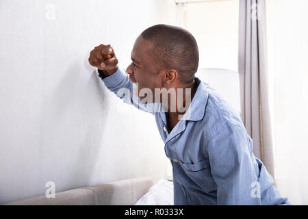 Aggressivo giovane uomo che colpisce la parete di suo pugno Foto Stock