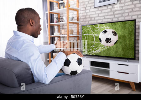 Scioccato African uomo seduto sul divano guardando la partita di calcio in televisione Foto Stock