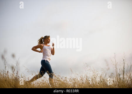 Ragazza adolescente che corre lungo una traccia in un campo. Foto Stock