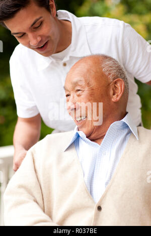 Senior uomo essendo spinto in una sedia a rotelle dalla sua balia. Foto Stock