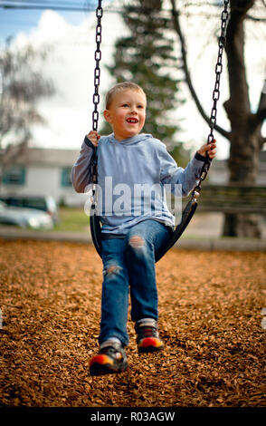 Giovane ragazzo giocando su un altalena in un parco. Foto Stock