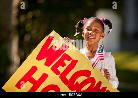 Giovane ragazza con una bandiera americana e un welcome home iscriviti. Foto Stock