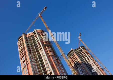 Gru per edilizia sulla costruzione di abitazione parallelamente due grattacieli. Serena giornata di sole Foto Stock