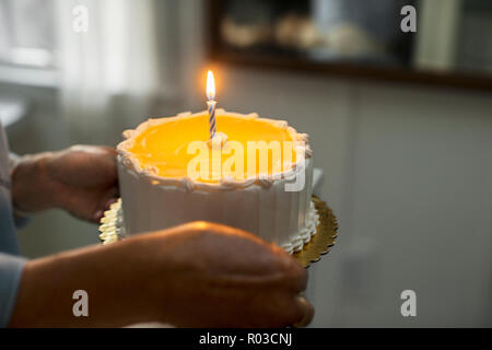 Le mani di una donna matura in possesso di una torta di compleanno. Foto Stock
