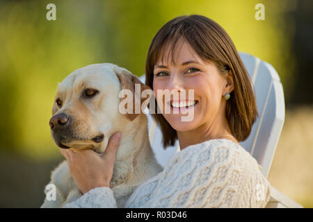 Ritratto di un sorridente ragazza rilassante con il suo cane su una sedia a sdraio in un giardino soleggiato. Foto Stock