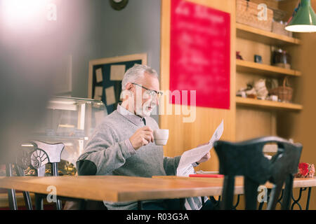 Barbuto imprenditore maturo leggendo il giornale e bere il caffè Foto Stock