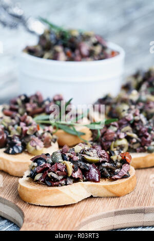 In casa oliva mescolato Tapenade fatta con aglio, capperi, olio d'oliva, Kalamata, olive nere e verdi sparsi su fette di pane abbrustolito. Profondità di campo Foto Stock