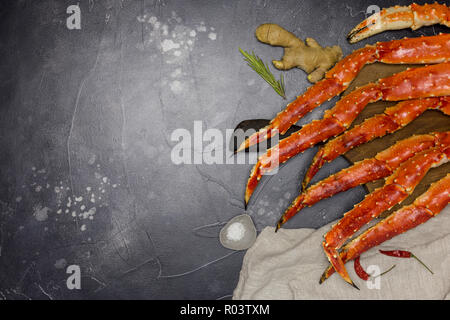 Re fresca kamchatka crab's claw con le fette di limone e zenzero, il sale e il rosmarino a tavola di legno, grigio igienico vicino su sfondo nero Foto Stock