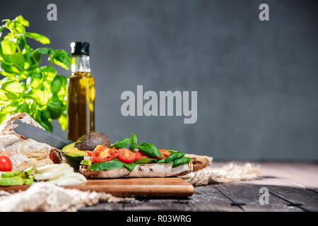 Sandwich freschi fatti di ciabatta pane, pomodori e avocado, mozzarella e basilico fresco sul tavolo rustico con ingredietns sullo sfondo. Orizzontale o Foto Stock