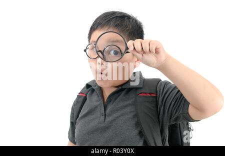 Felice scuola asiatica boy holding e guardando attraverso la lente di ingrandimento che mostra un occhio grande, isolato su sfondo bianco, il concetto di istruzione Foto Stock