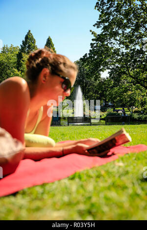 Essen, Germania, la zona della Ruhr, città giardino, giovane donna giace sul prato e legge in un libro Foto Stock