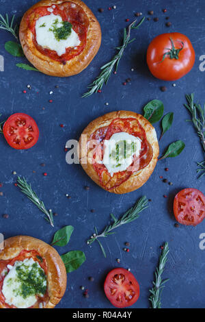 Tre in casa mini pizza con pomodori, formaggio e pancetta, lesioni e spezie su sfondo scuro in verticale Foto Stock