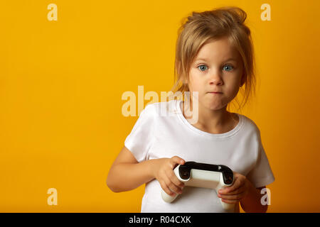 Poco assorbiti ragazza in t-shirt bianco tenendo un game pad la riproduzione del video gioco su sfondo giallo Foto Stock