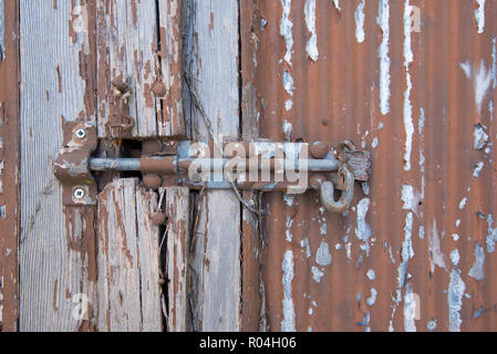 Un arrugginito dipinto bullone scorrevole è fissato con un lucchetto Lockwood e un embedded serratura a chiave in una vecchia porta di legno con peeling paint Foto Stock