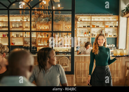 Sorridente cameriera portare bevande da persone sedute in un bar Foto Stock