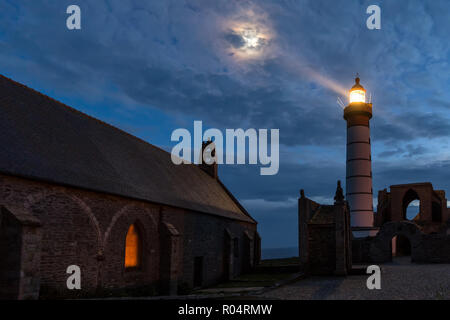 Chusrch mistico e faro illuminato con luna oltre il cielo nuvoloso a Saint Mathieu punto, Brittany, Francia Foto Stock
