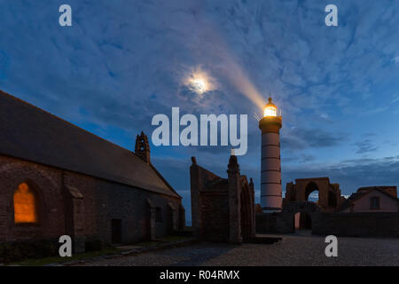 Chiesa mistica e faro illuminato con luna oltre il cielo nuvoloso a Saint Mathieu punto, Brittany, Francia Foto Stock