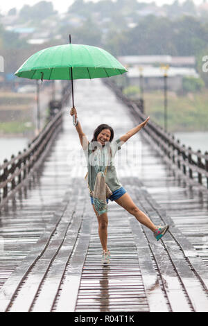 Woman Dancing sotto la pioggia caduta sul Mon ponte di legno di Sangklaburi, Thailandia Foto Stock