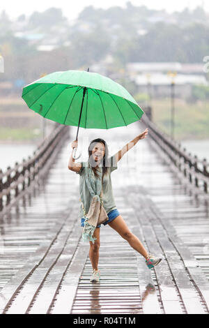 Woman Dancing sotto la pioggia caduta sul Mon ponte di legno di Sangklaburi, Thailandia Foto Stock