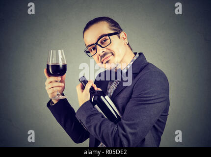 Funny Man in tuta e occhiali abbracciando una bottiglia di vino di contenimento essendo wineglasses addicted ad alcool Foto Stock