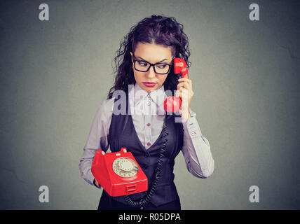 Giovane donna che guarda confuso e dubbioso mentre si parla sul telefono rosso contro lo sfondo grigio Foto Stock