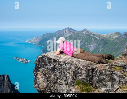 Donna guarda sul fiordo Örnfjord verso isola Husöy, la cima della montagna Grytetippen, isola Senja, Troms, Norvegia Foto Stock