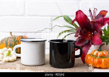 Due bianco e nero smalto campfire tazza da caffè mockup con caduta di ringraziamento arancione zucca e giglio rosso. Boccale vuoto mock up per la promozione del design. Foto Stock