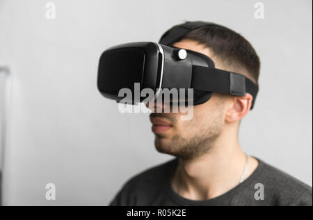 Giovane uomo che indossa la realtà virtuale gli occhiali di protezione auricolare, casella di vr e seduta in ufficio contro il monitor del computer. Il collegamento, la tecnologia di nuova generazione, il concetto di progresso. Foto Stock