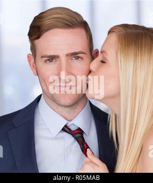 Close-up di una giovane donna tirando un giovane uomo verso di lei con il suo tirante baciando la guancia Foto Stock