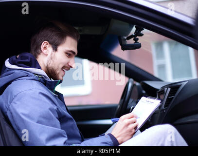 L'uomo firma un documento mentre è seduto in macchina Foto Stock