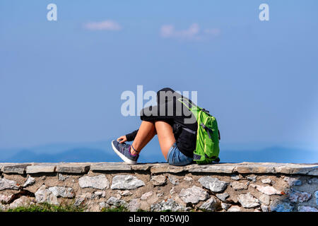 Un uomo con un zaino verde siede su un muro di pietra e rilassa. Foto Stock