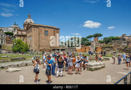 Un gruppo turistico al Foro Romano contro lo sfondo della Curia Julia, un Senato della città antica di Roma Foto Stock