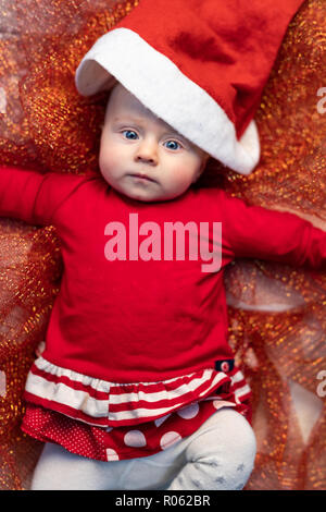 Little baby in una festosa red Santa outfit giacente su un oro tessuto glitter per celebrare il Natale visto dal di sopra Foto Stock