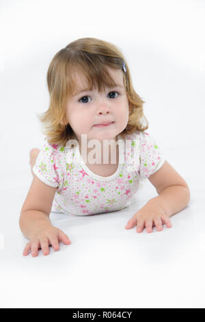 Giovane carina ragazza caucasica strisciare in avanti sul suo stomaco verso il fotografo. Una verticale di colore pieno close up immagine girato in uno studio. Foto Stock